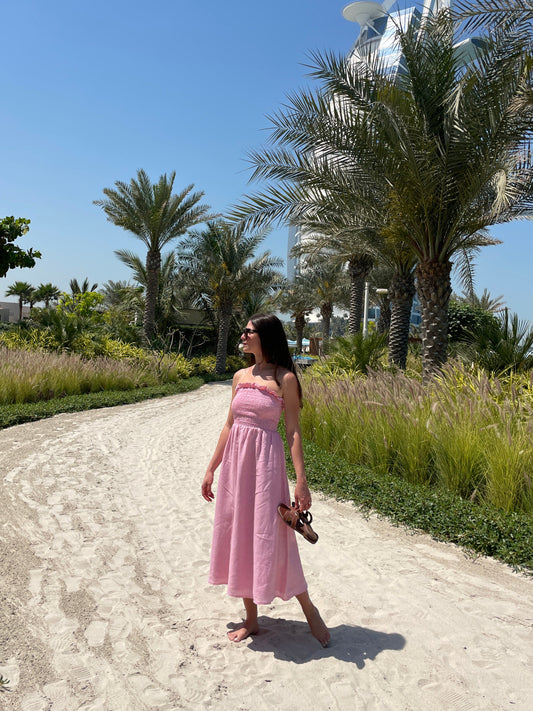 Woman in a pink dress standing on a sandy path with palm trees in the background
